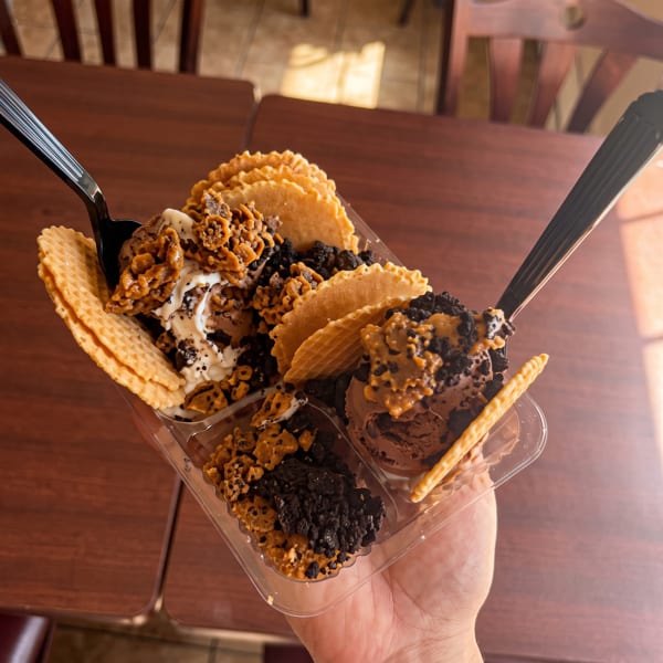 Hand holding a clear plastic container with chocolate ice cream, waffle crisps, and toppings.