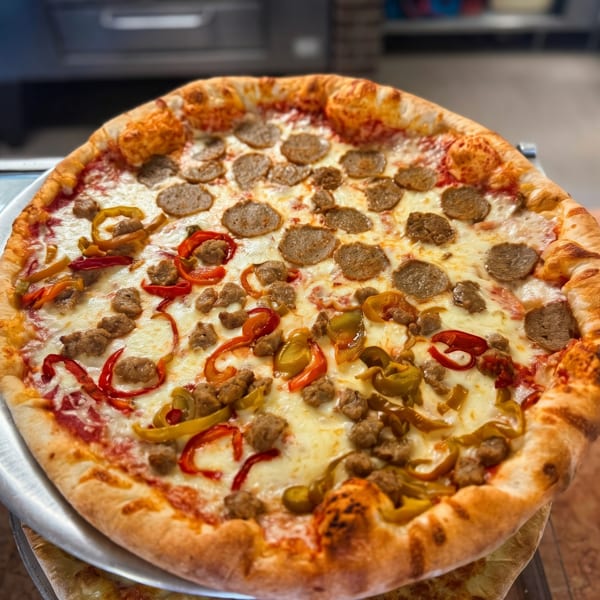 A whole pizza with sausage, pepperoni, and red and yellow bell peppers on a metal tray.